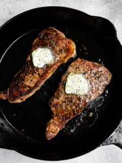 cast iron strip seared strip steak in a pan with butter on top