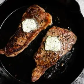cast iron strip seared strip steak in a pan with butter on top