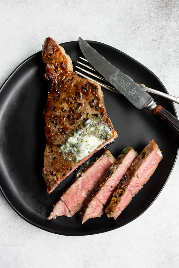 sliced cast iron seared strip steak on a black plate