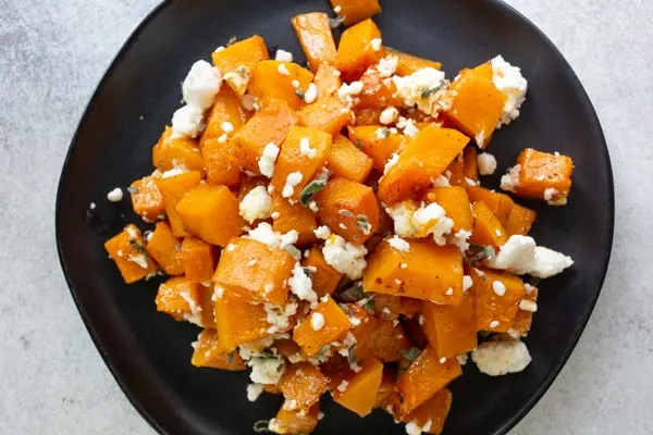 honey roasted butternut squash on a black plate sprinkled with goat cheese