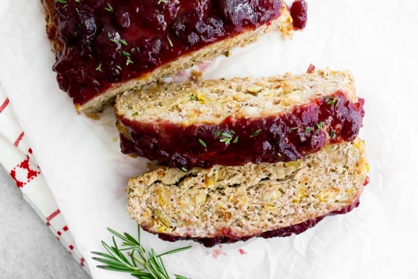 Sliced Thanksgiving turkey meatloaf surrounded by fresh herbs