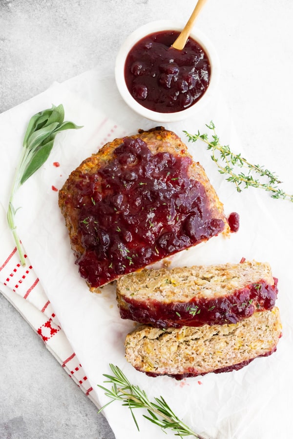 Thanksgiving turkey meatloaf sliced and staged with fresh herbs and extra cranberry sauce.