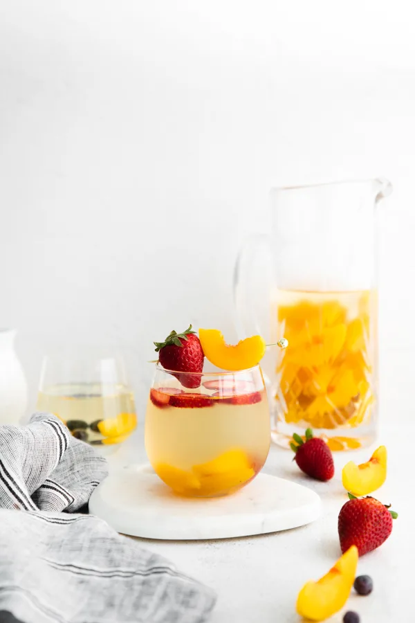 white wine peach sangria in a glass with peach slices and strawberries.