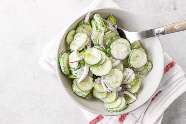 creamy horseradish cucumber salad in a ceramic bowl with a wooden spoon. 