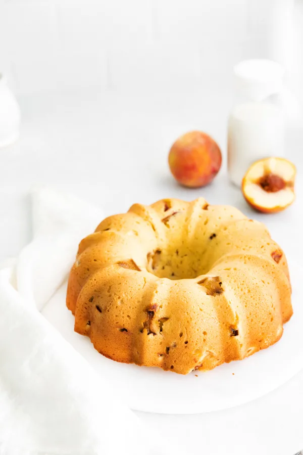 Peach Bundt Cake on a cake plate with some fresh peaches in the background. 