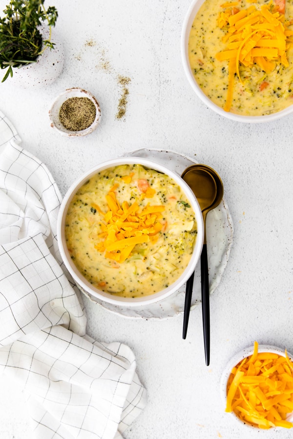 Instant Pot Broccoli Cheddar Soup in a white serving bowl set on a plate. 