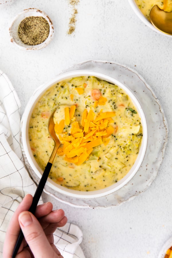 Instant Pot Broccoli Cheddar Soup in a bowl with a hand holding a spoon in the soup. 