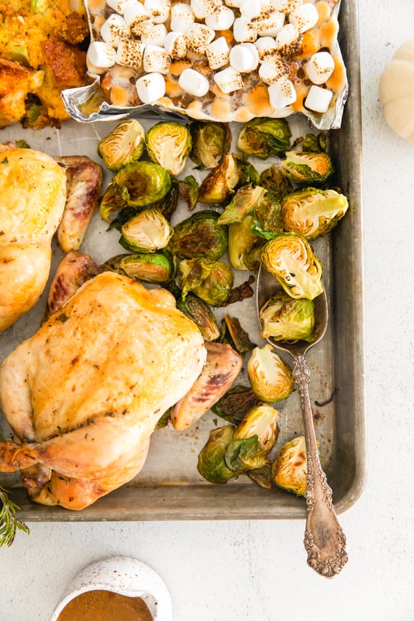 Sheet Pan Thanksgiving Dinner on a sheet pan with a spoon scooping up Brussels sprouts. 
