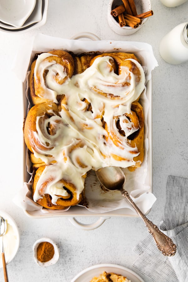 Gingerbread Cinnamon Rolls in a dish topped with frosting. 