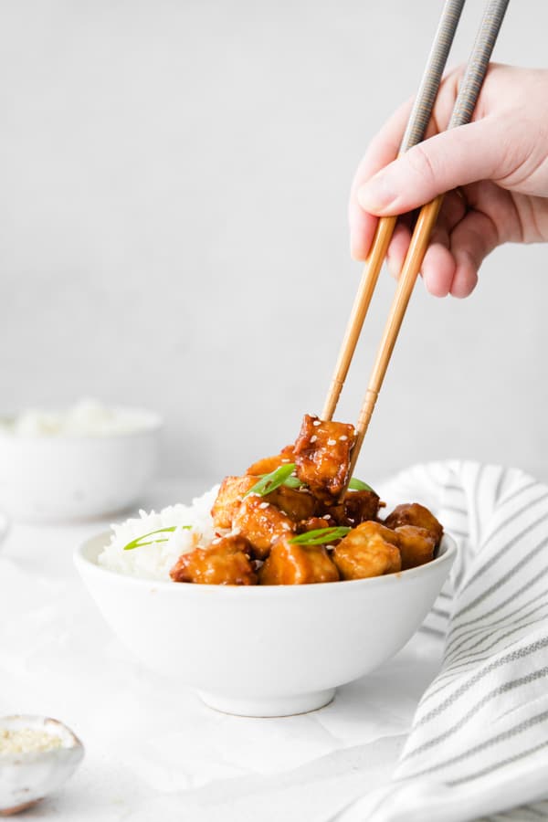 A person holding chopsticks taking a bite of Air Fryer Sweet Chili Tofu. 