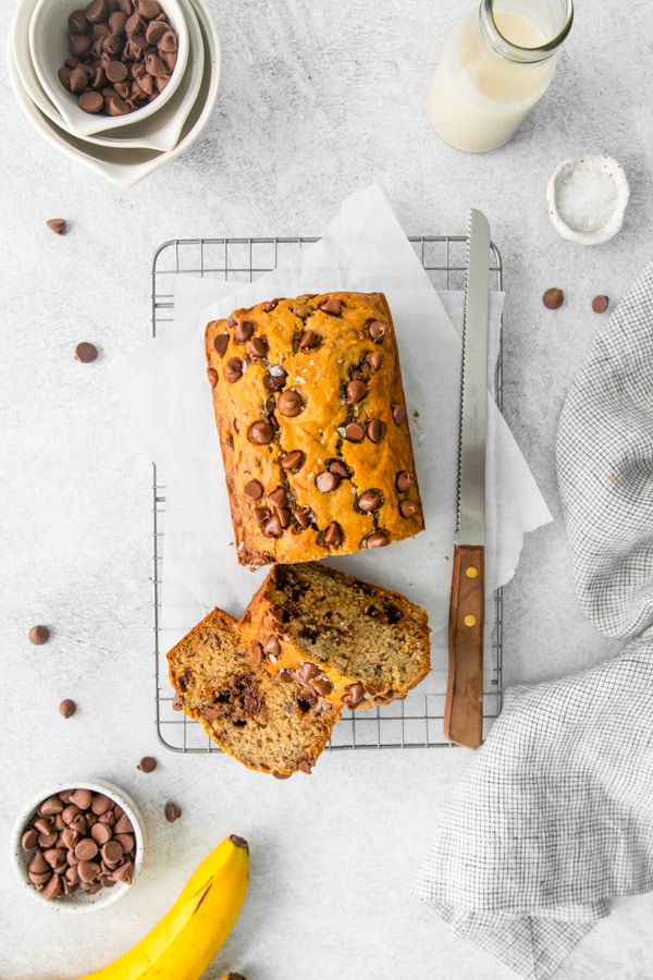 Chocolate Chip Banana Bread surrounded by ingredients and extra chocolate chips. 