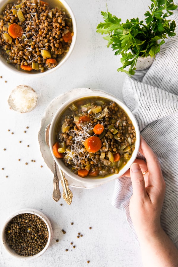 a hand holding a bowl of Healthy French Lentil Soup. 