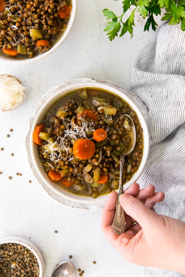 Healthy French Lentil Soup in a bowl with a hand going in for a spoonful. 