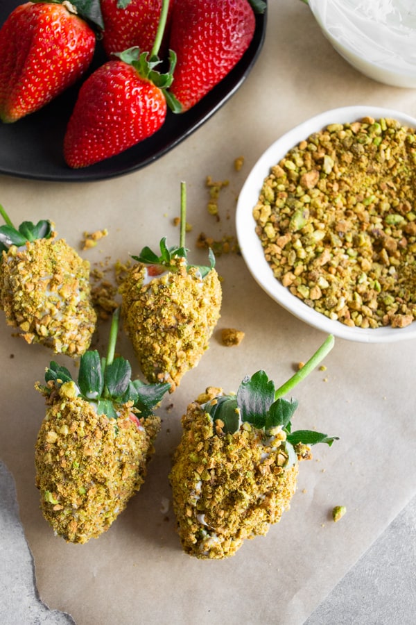 Pistachio White Chocolate Covered Strawberries sitting on parchment paper with crushed pistachios. 