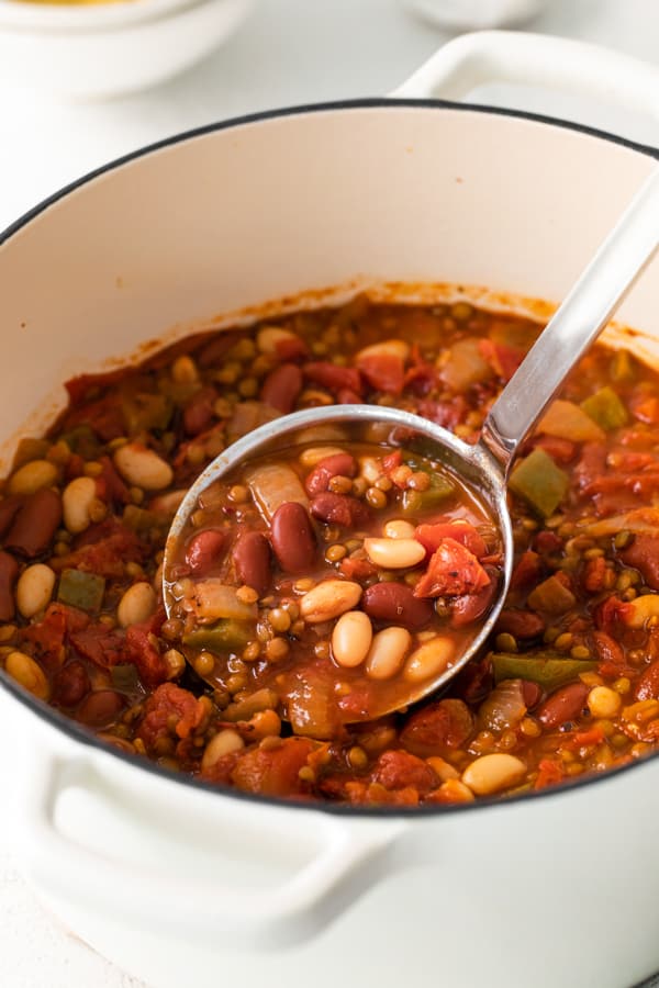 A ladle of Vegan Lentil Chili being taking out of a soup pot. 