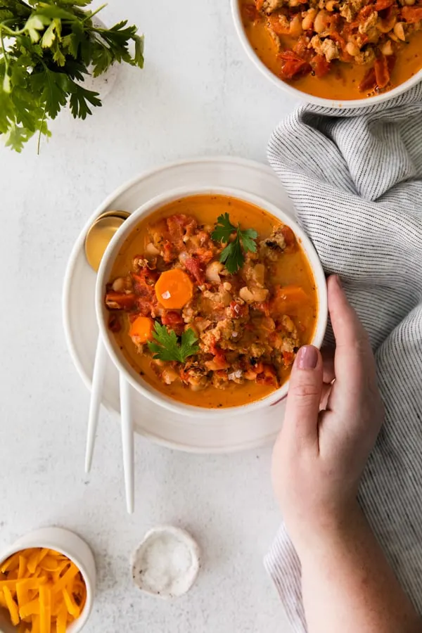 Instant Pot Ground Chicken Chili in a bowl with a hand holding the bowl of soup. 