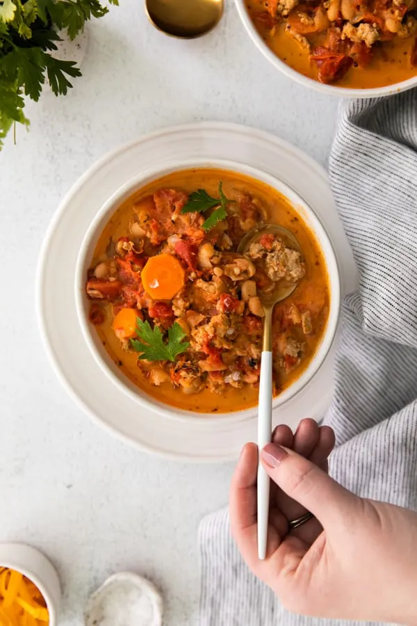Instant Pot Ground Chicken Chili in a bowl with a person holding a spoon in the soup. 