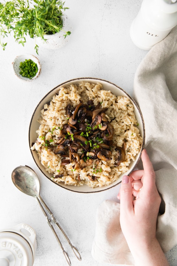 Wild Mushroom Risotto in a bowl with a hand going in to grab the bowl. 