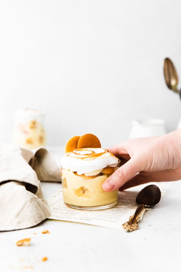 A hand picking up a single serve glass of The Best Banana Pudding. 
