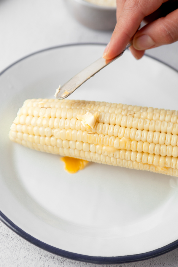 Butter being spread onto a cob of corn. 