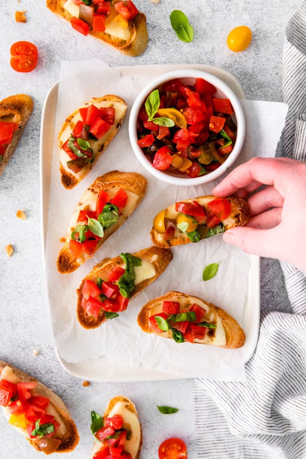 A hand grabbing a pice of Caprese Bruschetta. 