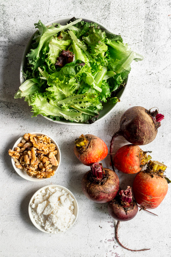 a bowl of lettuce, beets, walnuts, and feta cheese on a table. 