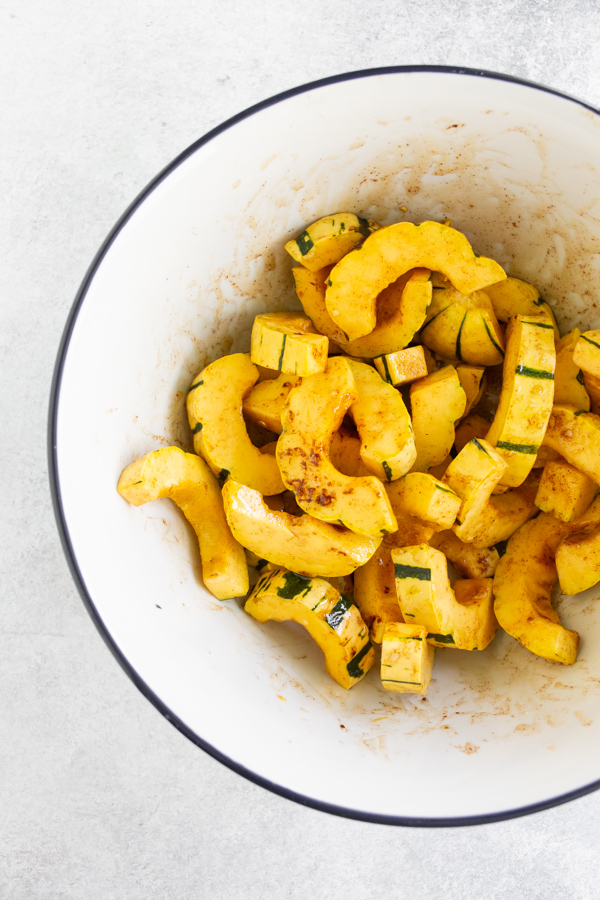 Sliced delicata squash in a bowl mixed with ingredients before roasting. 