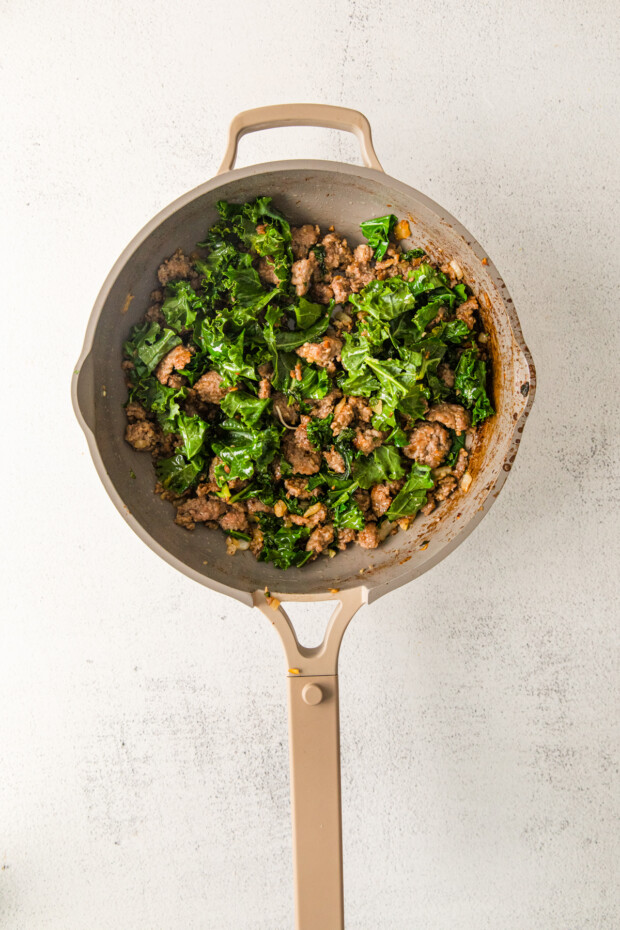 Sausage and kale cooking in a skillet. 