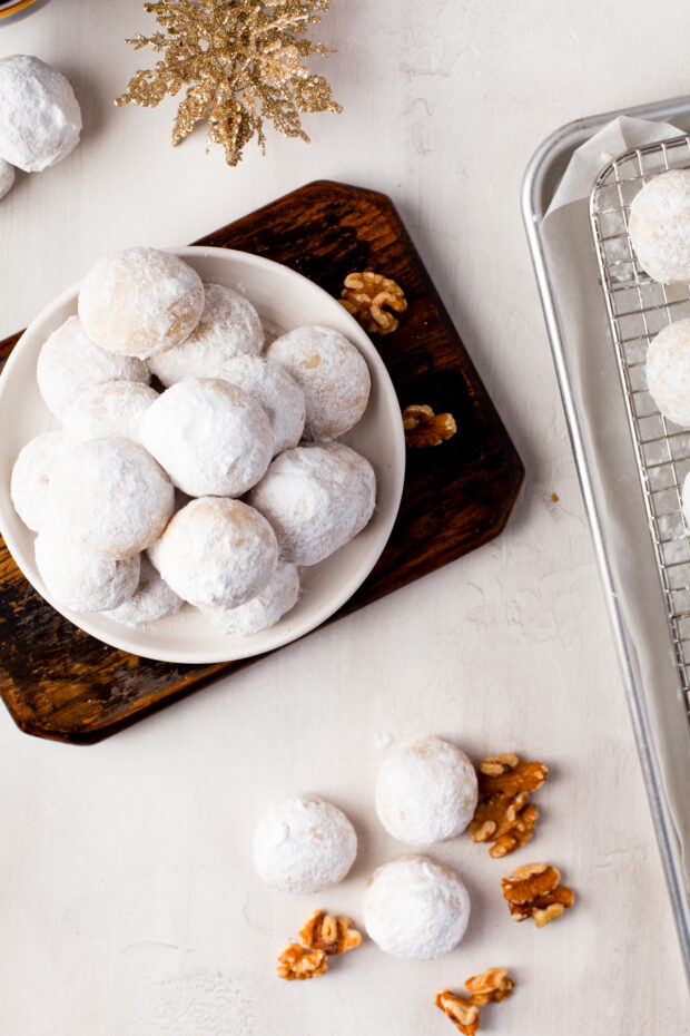Snowball Cookies on a table with a plate of cookies next to it. 