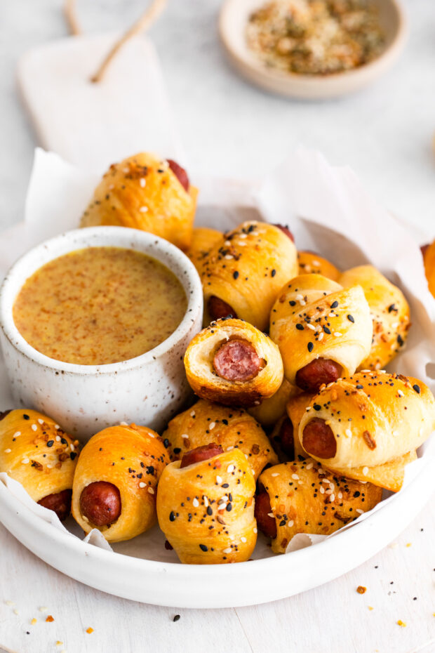 Everything Bagel Pigs in a Blanket served in a dish with sauce. 