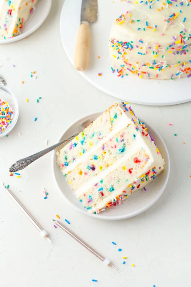 A sliced of confetti layer cake on a white plate. 