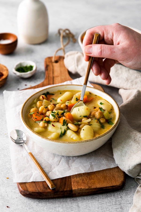 Vegetable Gnocchi Soup in a bowl with a hand holding a spoon going for a bite. 