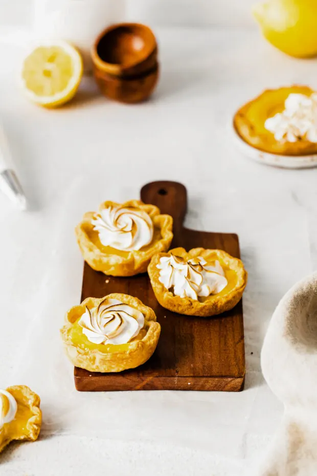 Mini Lemon Meringue Tarts on a cutting board topped with meringue. 