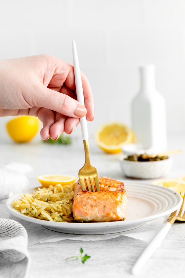 A hand holding a fork going into a piece of pan seared salmon. 