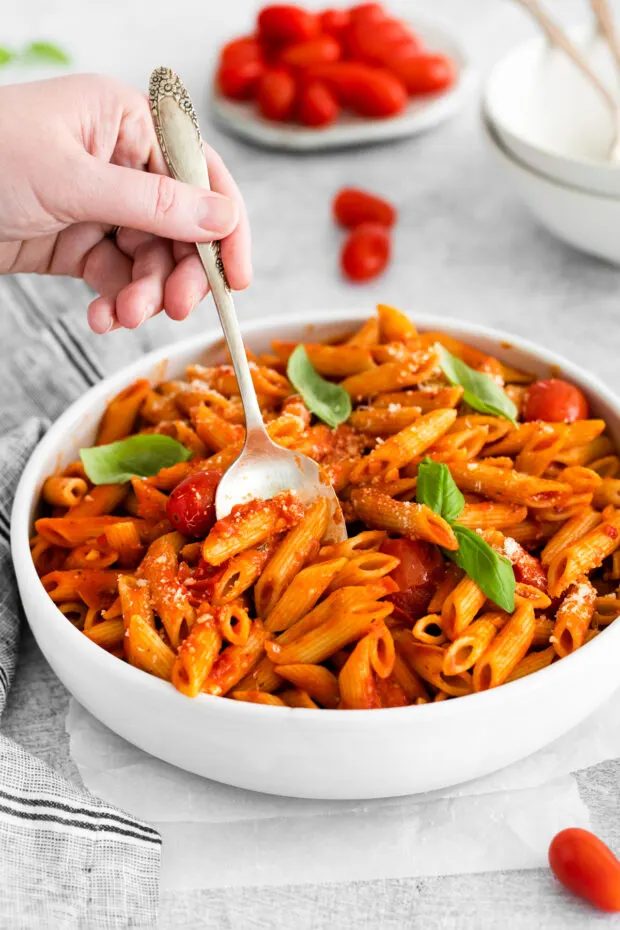A spoon taking some Penne Arrabbiata out of a serving bowl. 