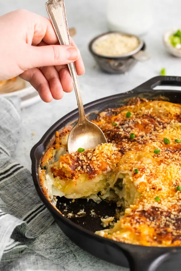 Taking a serving of scalloped potatoes out of a cast iron skillet. 