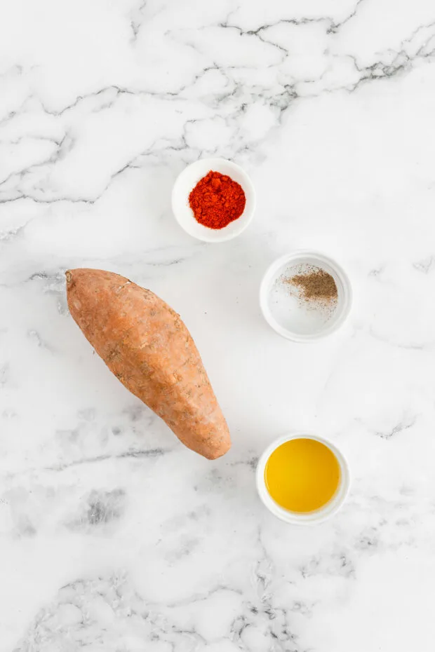 A sweet potato, spices, and olive oil on a table. 