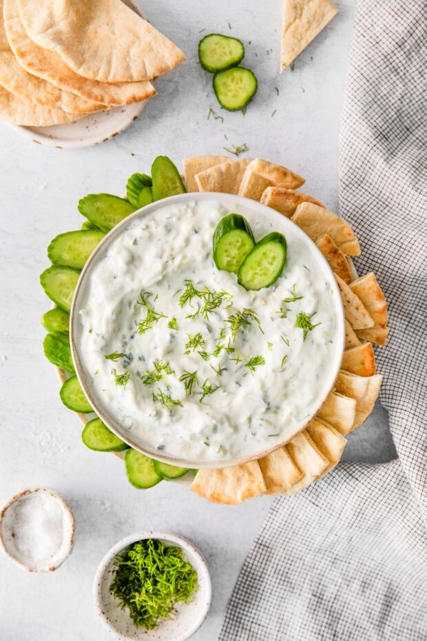 Tzatziki Sauce in a bowl surrounded by cucumber and pita bread. 