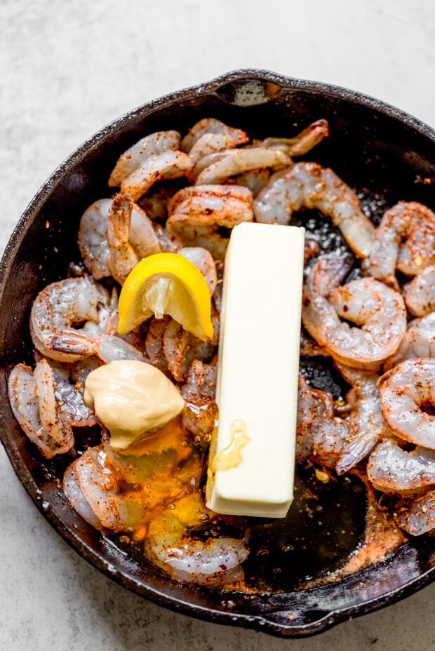 Seasoned shrimp in a pan with a stick of butter. 