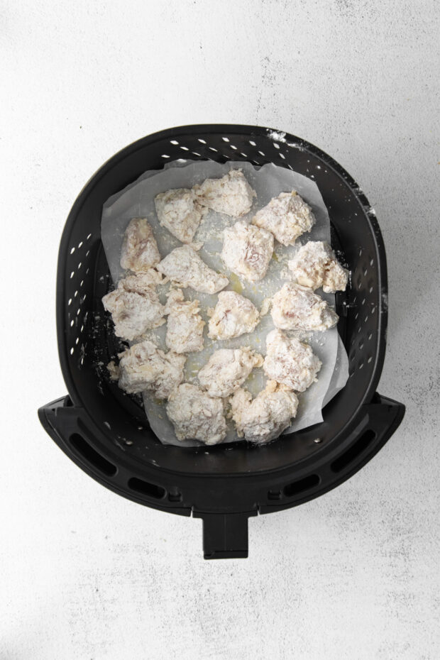 Floured chicken nuggets in an air fryer basket. 