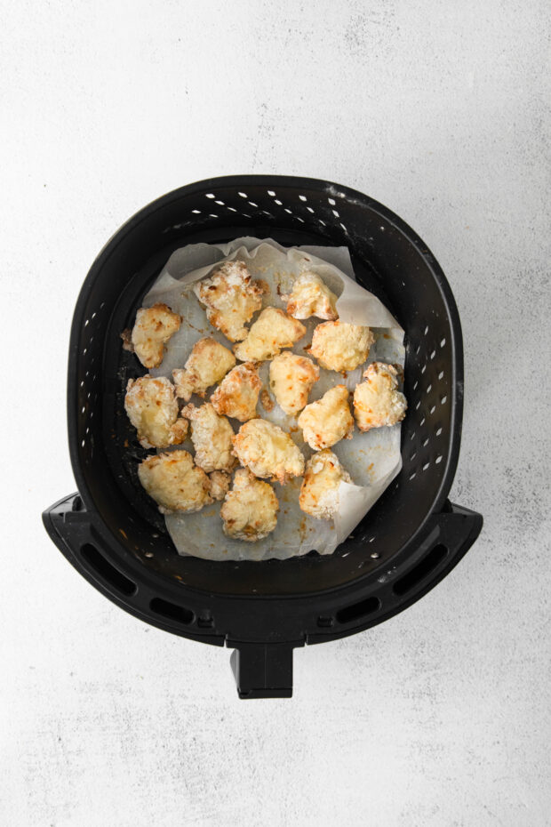 Cooked chicken nuggets in an air fryer basket. 