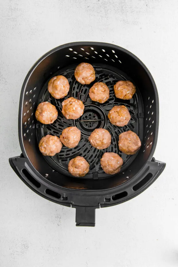 Uncooked air fryer chicken meatballs in a air fryer basket. 
