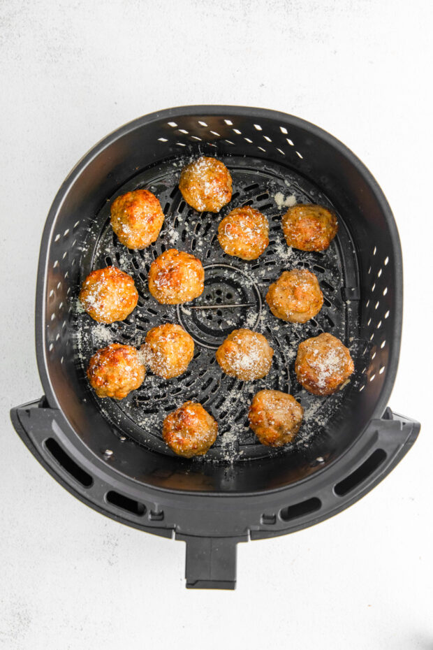 Cooked chicken meatballs in an air fryer basket. 