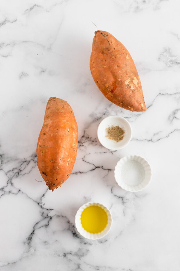 Sweet poatoes, salt, pepper, and oil on a table. 