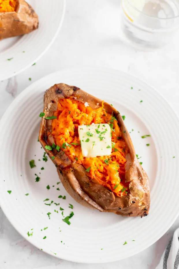 Baked Sweet Potatoes on a plate with herbs and butter. 