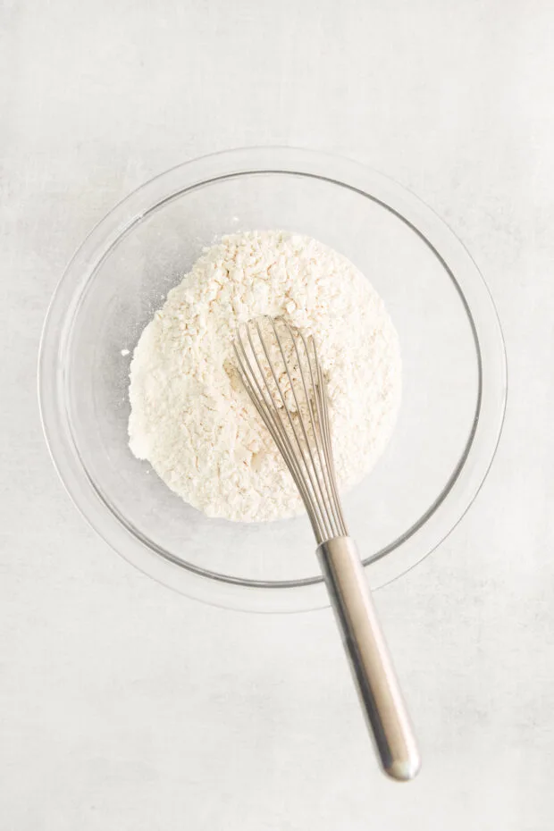 A bowl of flour with a whisk. 