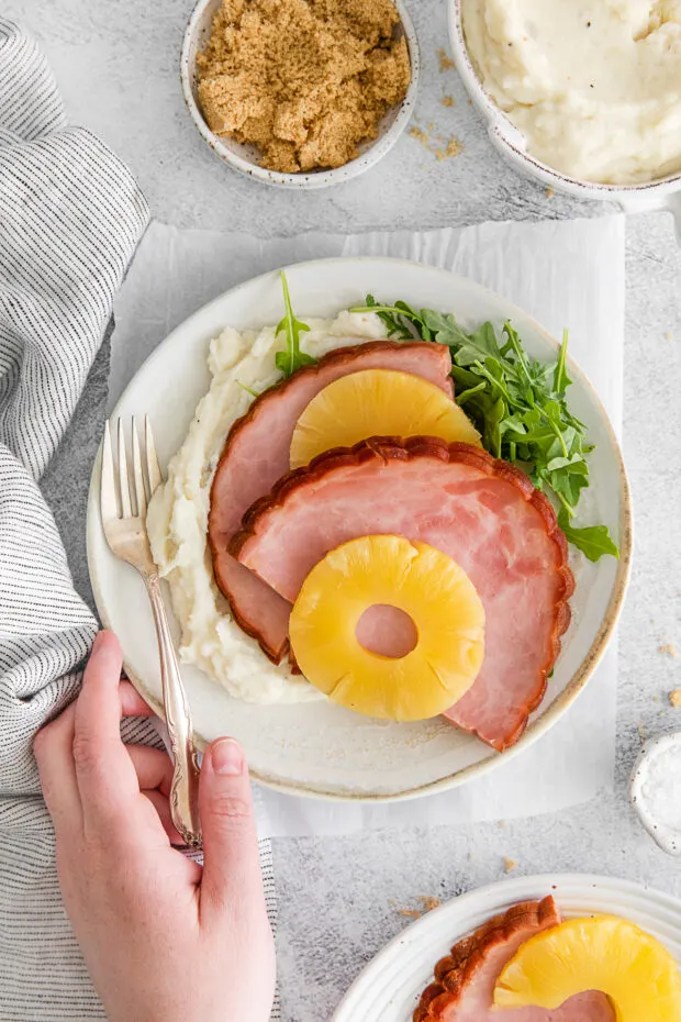 3-Ingredient Instant Pot Ham on a table with a hand holding the plate. 