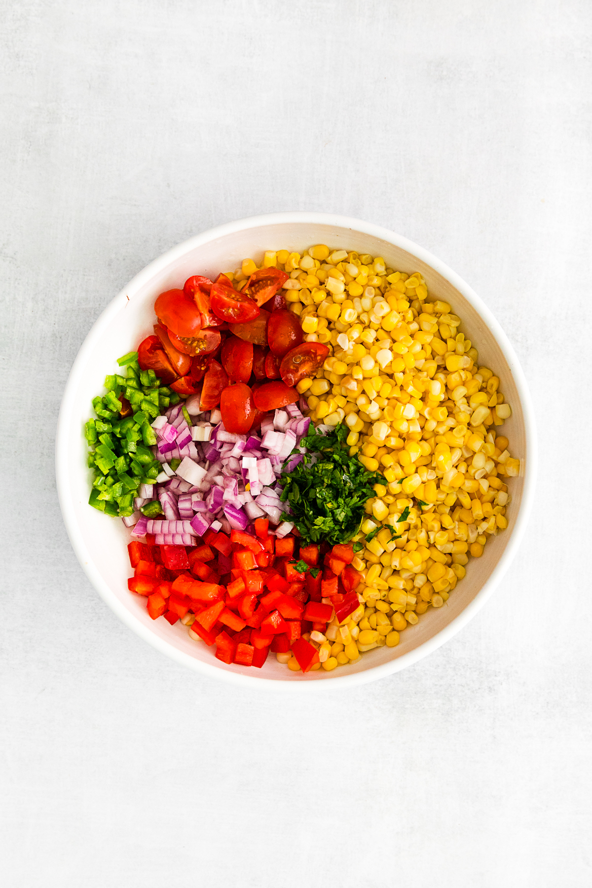 Corn, cilantro, tomatoes, red bell pepper, jalapeno and red onion in a bowl. 