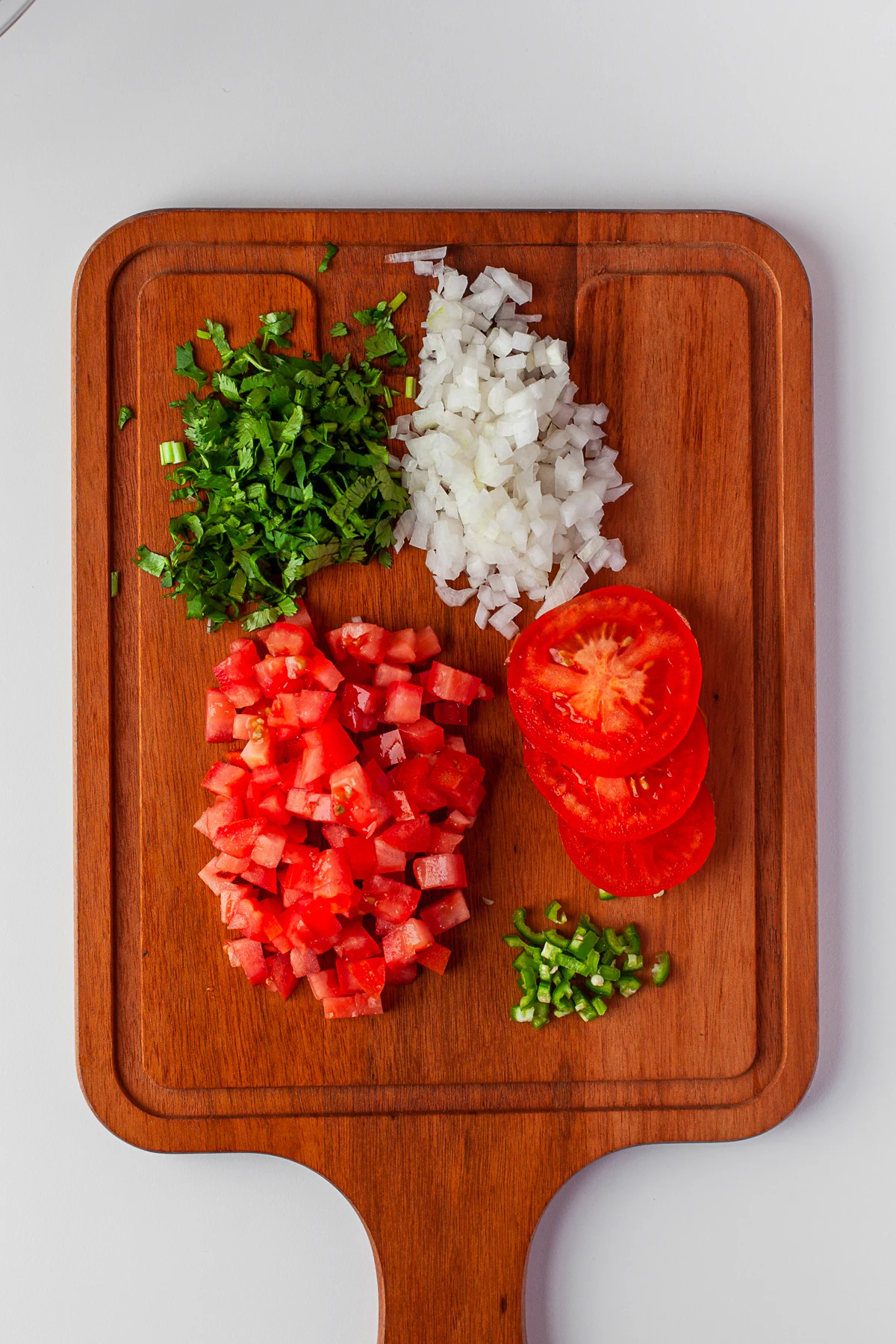 Chopped tomatoes, cilantro, onion, and chilies on a cutting board. 