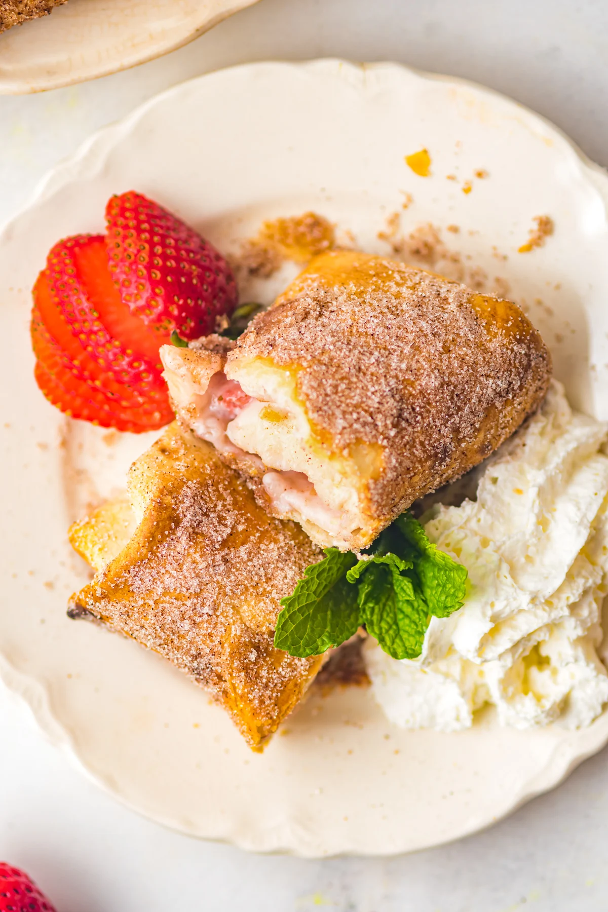 Air Fryer Strawberry Cheesecake Chimichangas cut in half and served with whipped cream. 